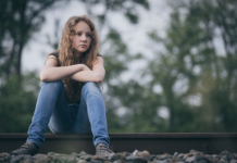 Nuori, surullinen tyttö istuu junaraiteilla.