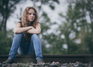 Nuori, surullinen tyttö istuu junaraiteilla.
