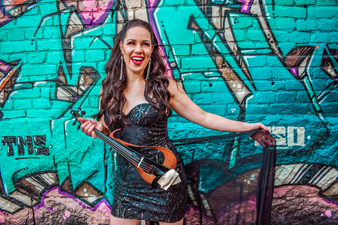 nuori nainen seisoo graffiteja täynnä olevan seinän edessä, kädessä viulu