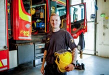 Tuomo Lahtinen seisoo palomiehen kypärä kädessään paloauton edessä.