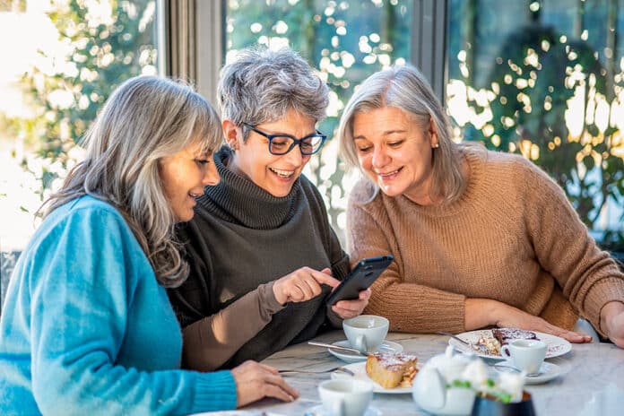 kolme iloista keski-ikäistä naista viettävät aikaa kahvilassa