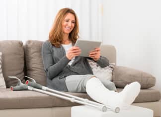 nainen istuu kipsi jalassa sohvalla kädessään tablettitietokone